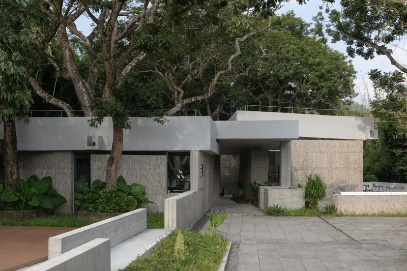 Street view of the concrete facade with textured stone panels beneath an overhanging canopy and mature trees