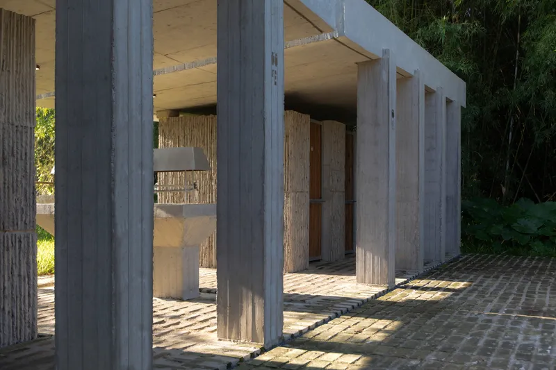 Colonnade of board-formed concrete columns casting diagonal shadows across a brick paver floor