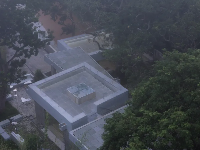 Aerial view of concentric square rooflines with central skylight in forested landscape