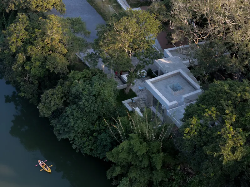 Drone view of the roof volumes with central pool terrace beside the water with kayakers below
