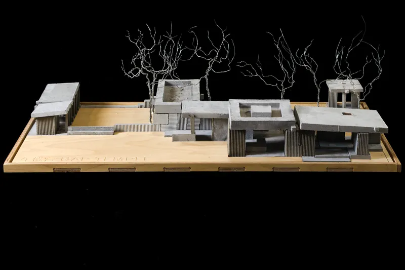 Physical model of clustered flat-roofed pavilions with wire trees against a black background