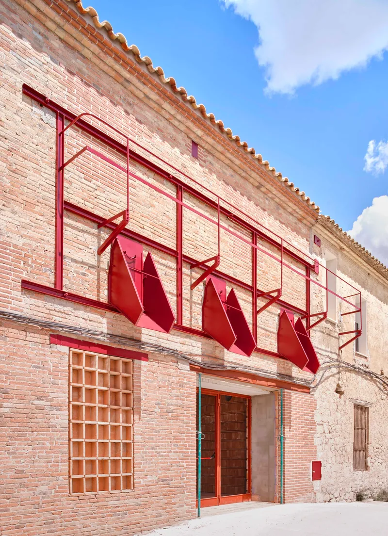 Brick facade with red metal awning frames and folded panels under a terracotta tile roof