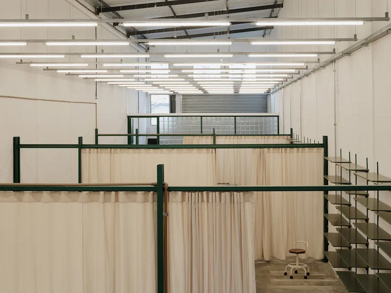 View through layered fabric partitions toward glazed mezzanine under grid of linear fluorescent fixtures