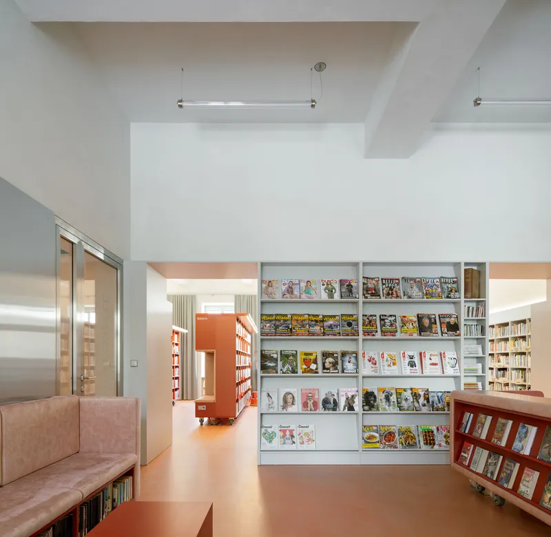 Library reading area with white magazine display shelves and coral rubber flooring under natural light
