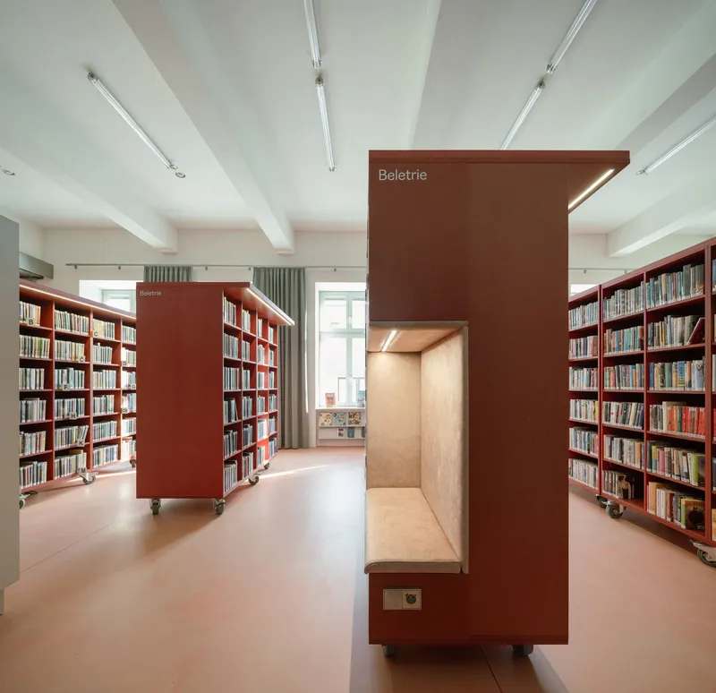 Freestanding coral booth with integrated bench seat flanked by mobile bookshelves on casters