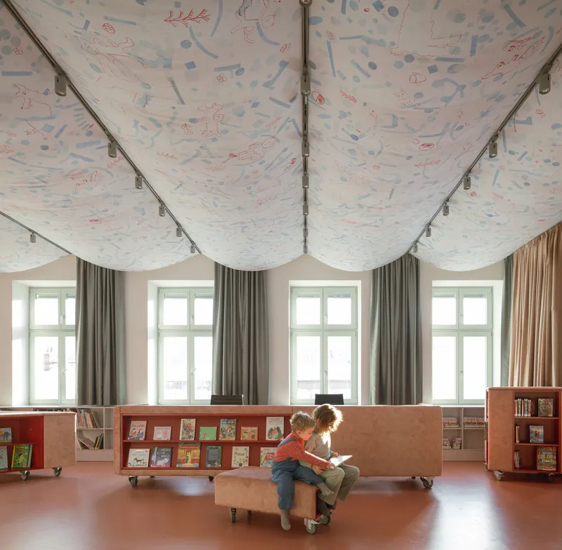 Children reading beneath a scalloped ceiling with hand-drawn illustrations in blue and coral