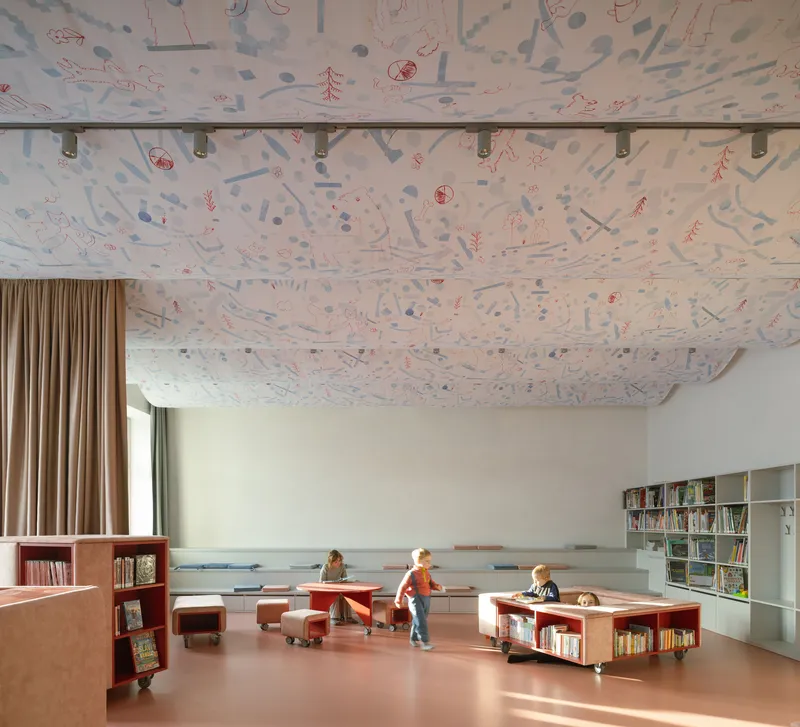 Library interior with illustrated fabric ceiling panels suspended over pink resin flooring with children playing