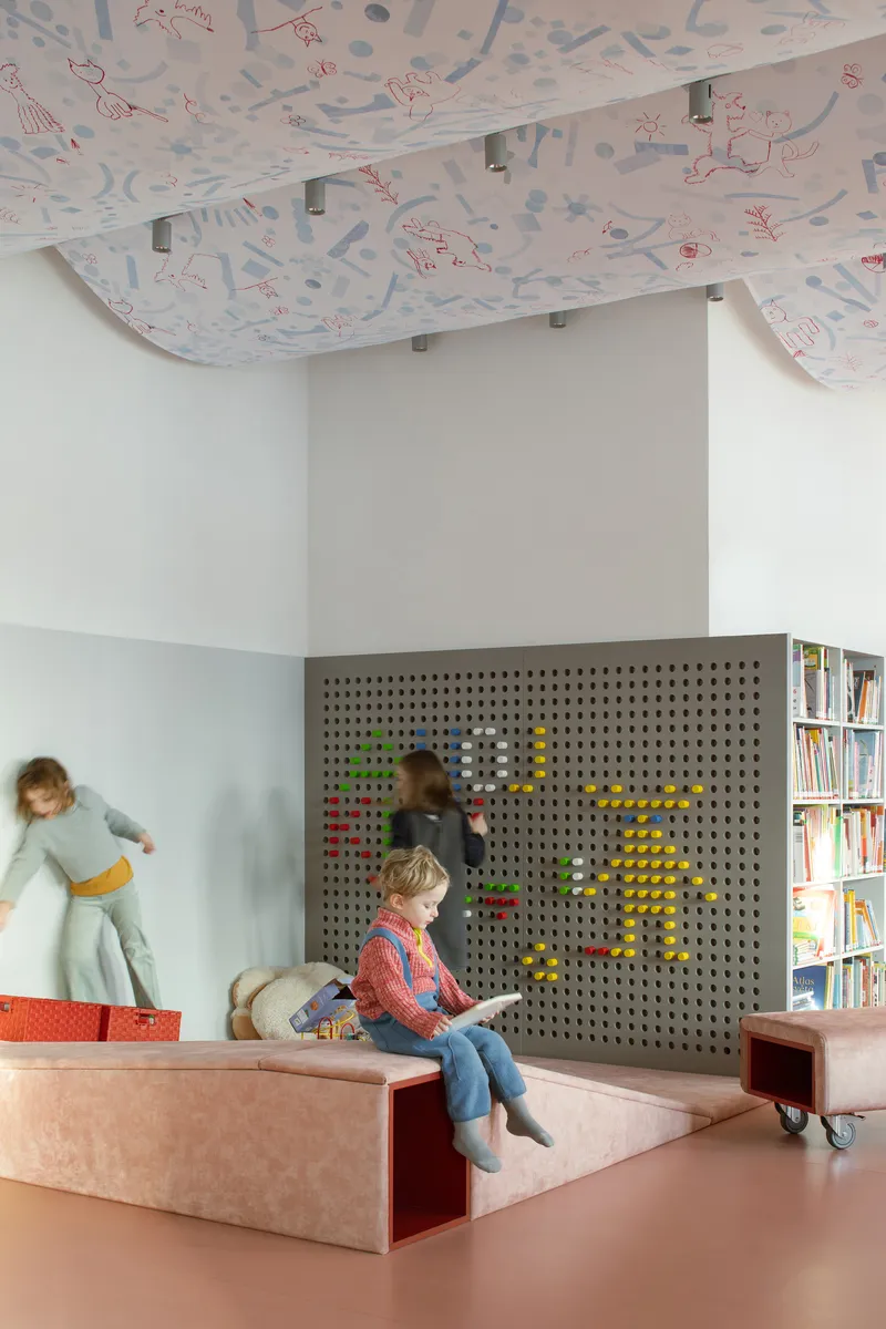 Pegboard wall with colored toys and children playing on stepped platform under draped illustrated ceiling