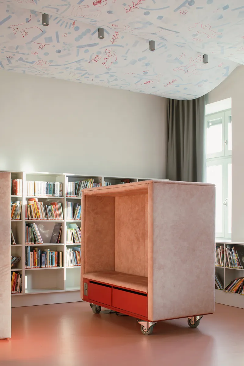 Mobile pink upholstered reading nook on casters with red storage drawer beneath scalloped ceiling panel