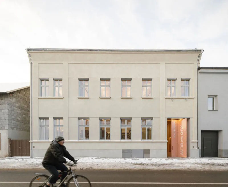 Street facade with pale plaster walls and symmetrical windows as a cyclist passes in winter