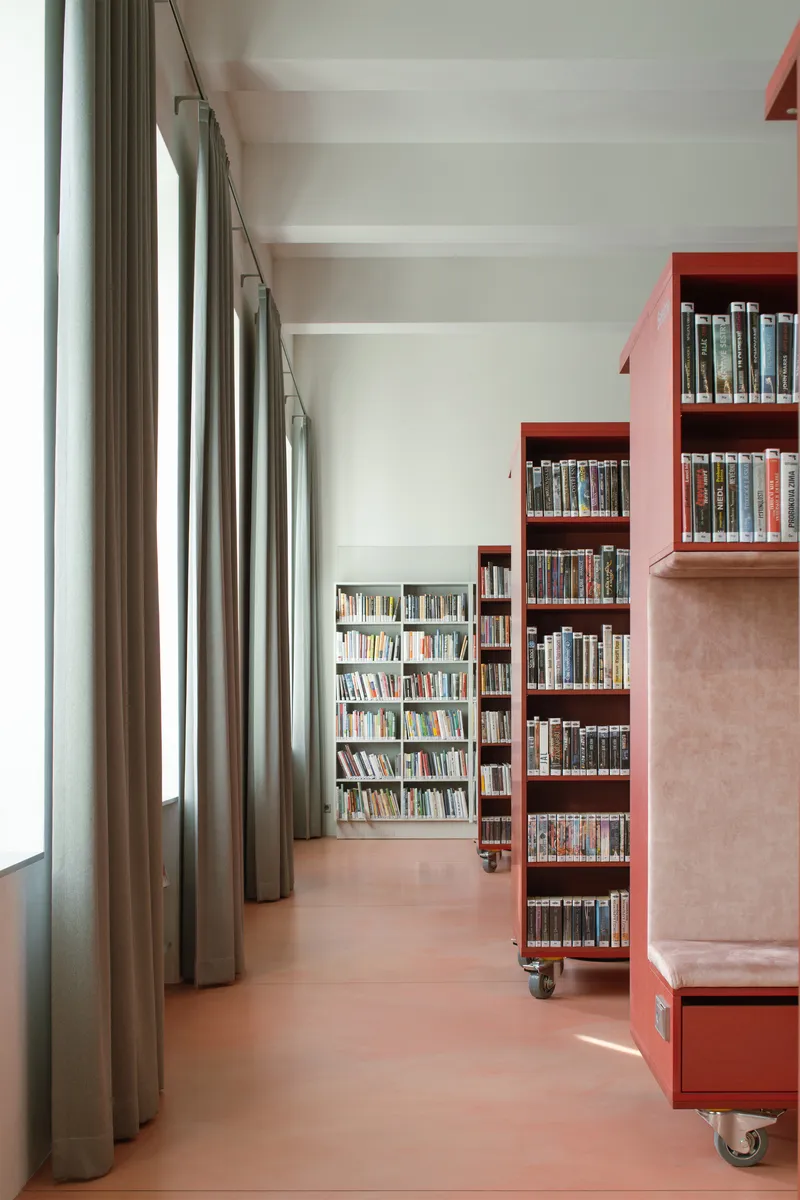 Interior corridor with floor-to-ceiling grey curtains, pink mobile shelving units, and terracotta flooring