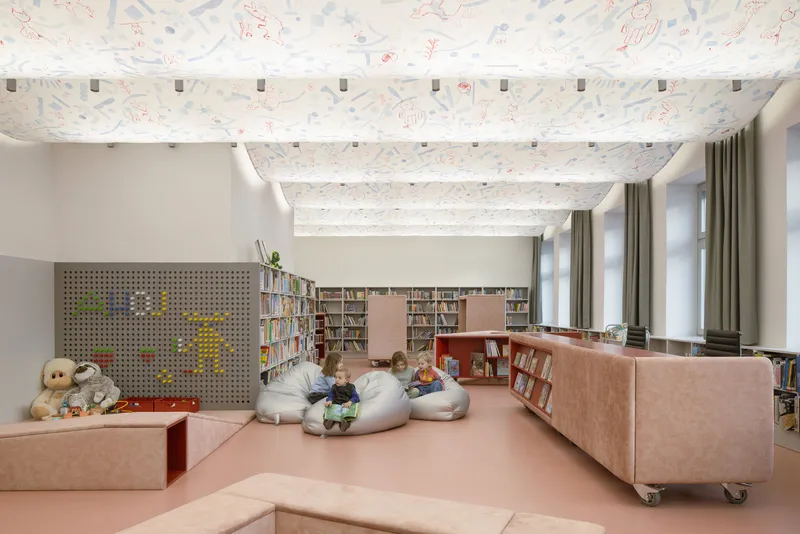 Reading room with patterned ceiling, exposed white beams, bean bag seating, and mobile pink bookshelves