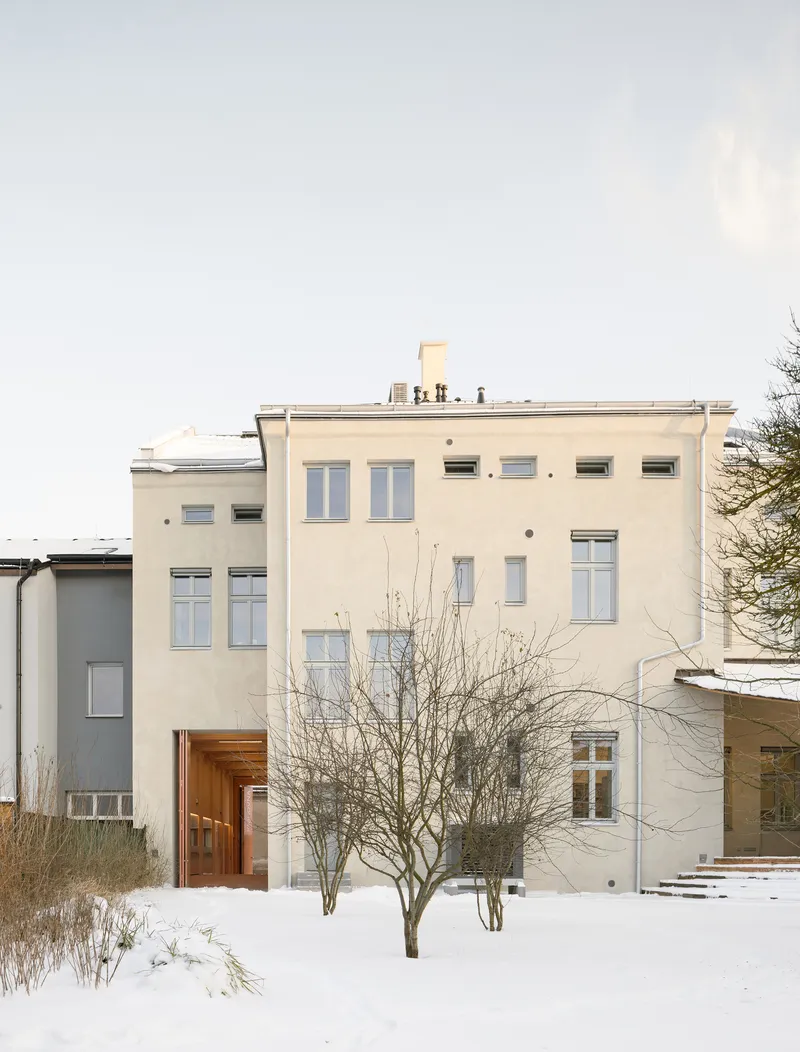 Rear elevation with pale stucco, varied window sizes, and bare winter trees in snow