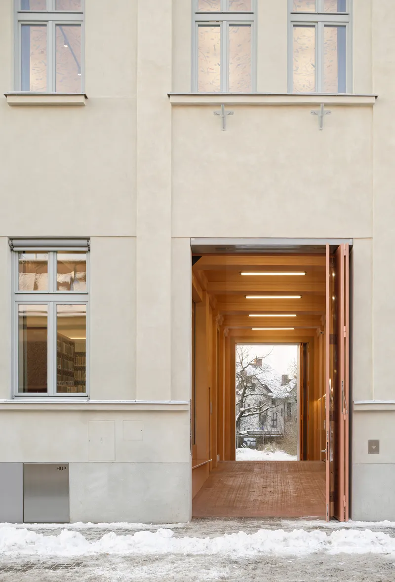 View through timber-lined entry vestibule with linear ceiling lights looking toward snowy courtyard