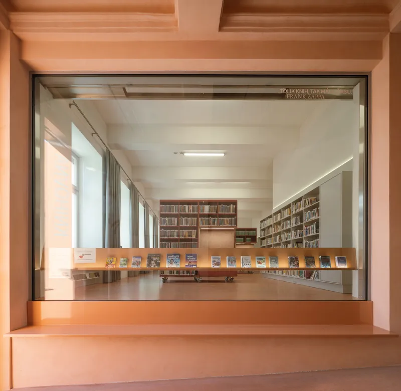 View through timber framed opening into library reading room with book display ledge and shelving