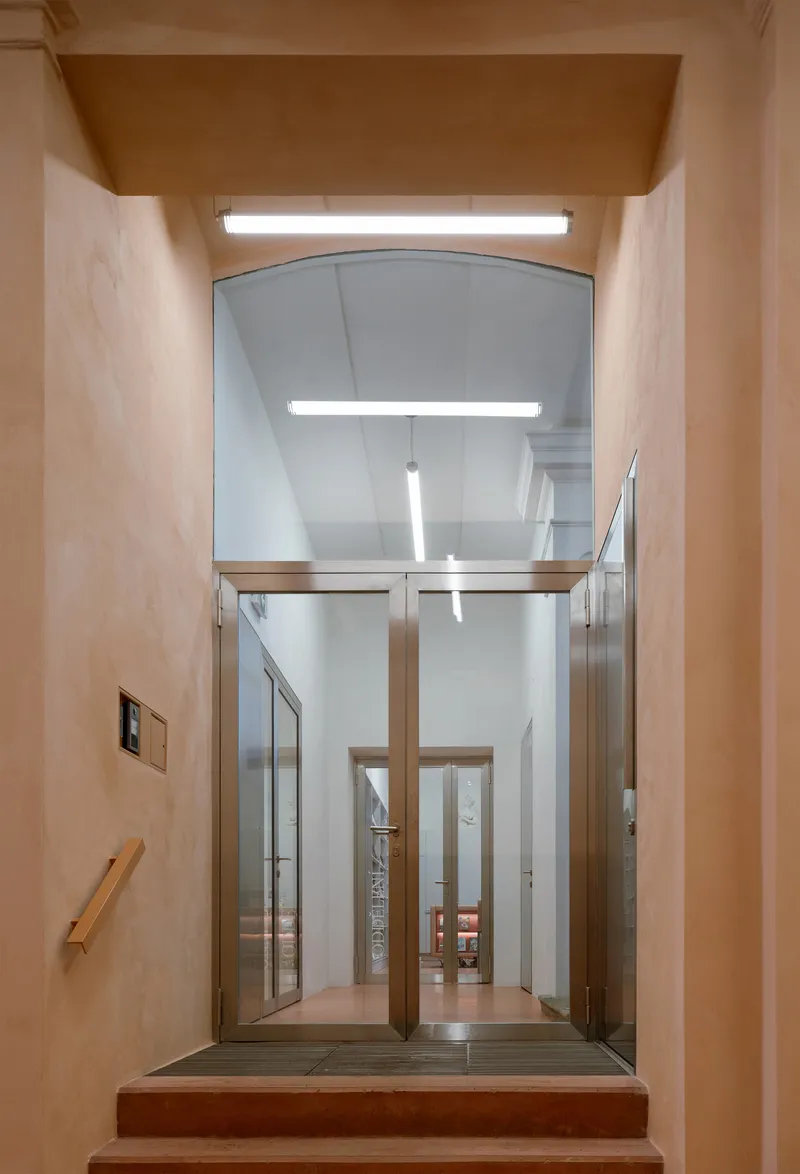 View through arched doorway showing glazed elevator cab beneath a plywood-clad ceiling alcove