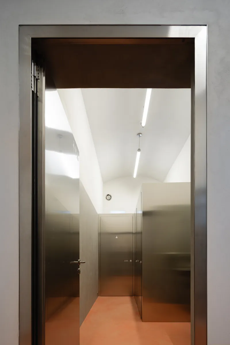 Corridor with polished stainless steel walls and terracotta floor beneath linear ceiling lights