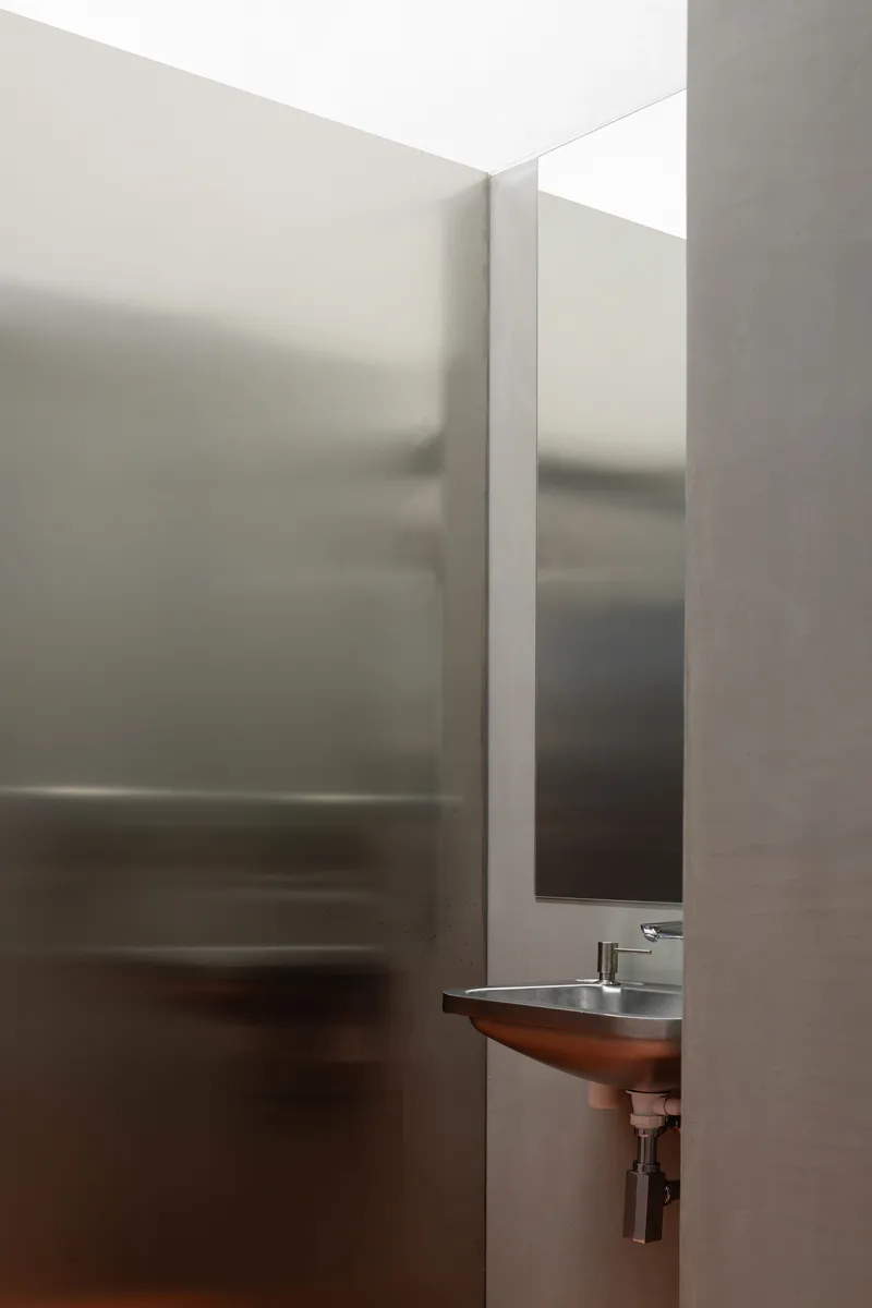 Translucent glass partition in bathroom with wall-mounted sink and vertical mirror slot