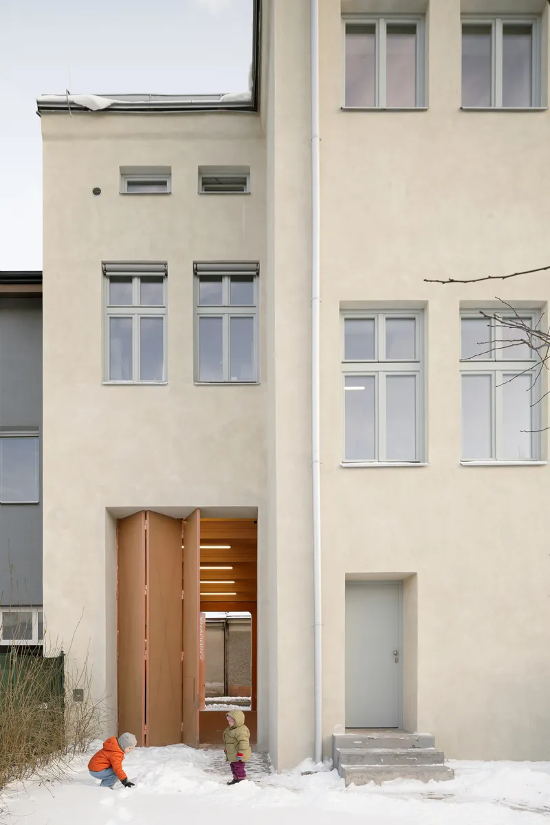 Street facade with cream plaster walls and tall vertical windows, children playing in winter snow