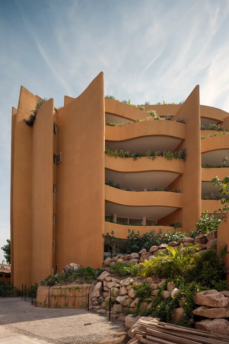 Curved balconies with planted beds cascading down the facade behind a rock garden at street level
