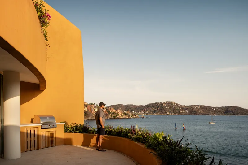 Rooftop terrace with outdoor kitchen overlooking a bay dotted with sailboats and hillside homes at dusk