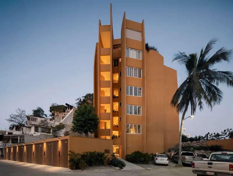 Street view of the ochre tower with vertical window openings lit from within at dusk