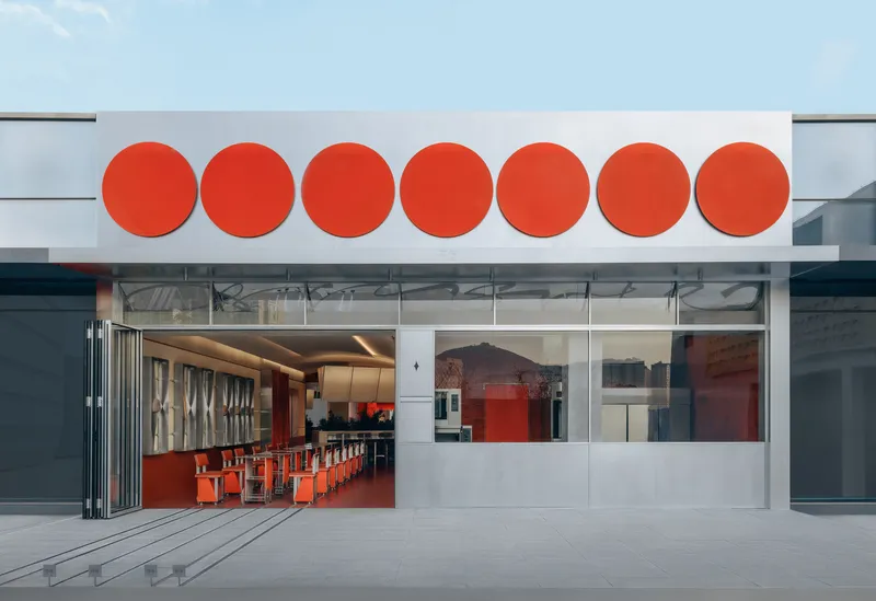 Facade with seven red circular motifs above folding glass doors opening to an interior with matching red seating
