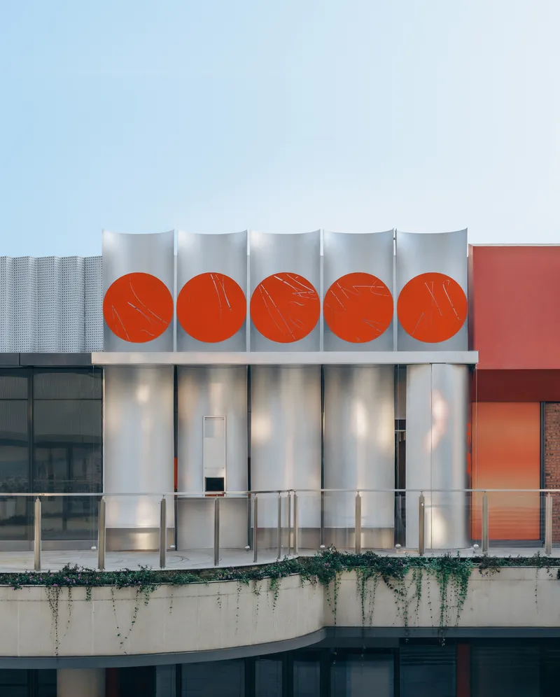 Translucent facade featuring five backlit red circles above a planted concrete terrace at dusk
