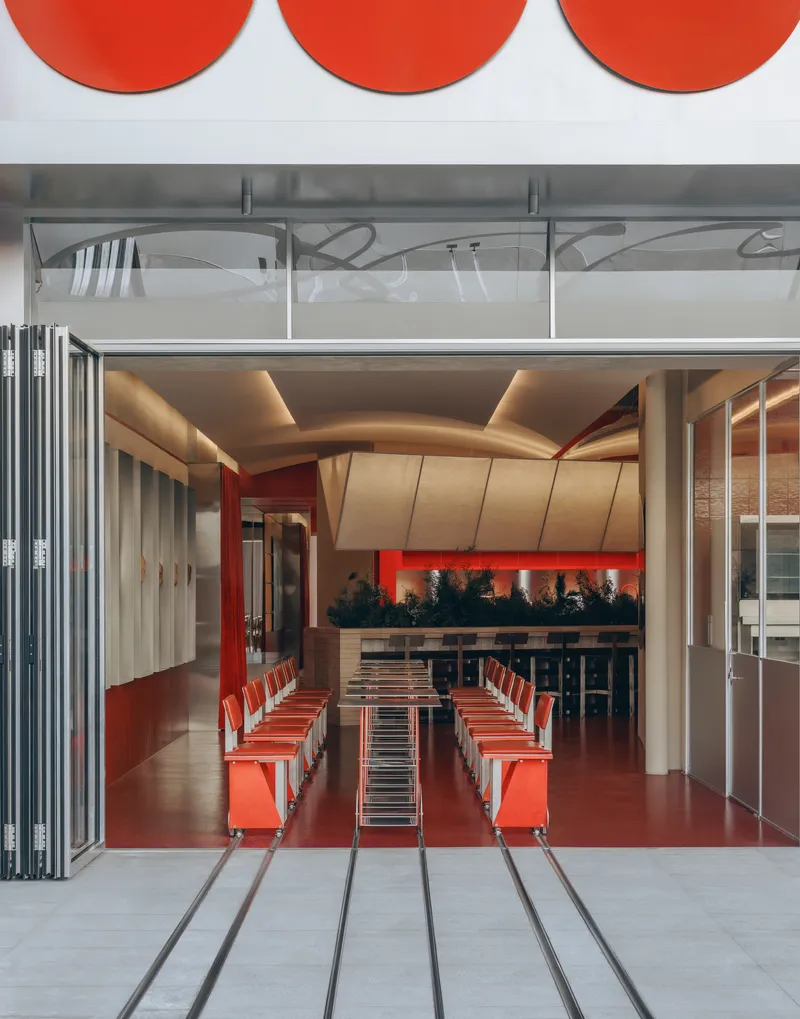 Interior view through open folding doors revealing a dining space with sculptural plywood ceiling and red flooring