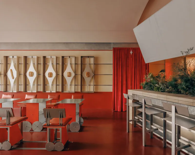 Interior dining area with red flooring, patterned wall screens, and raised planting bed with greenery