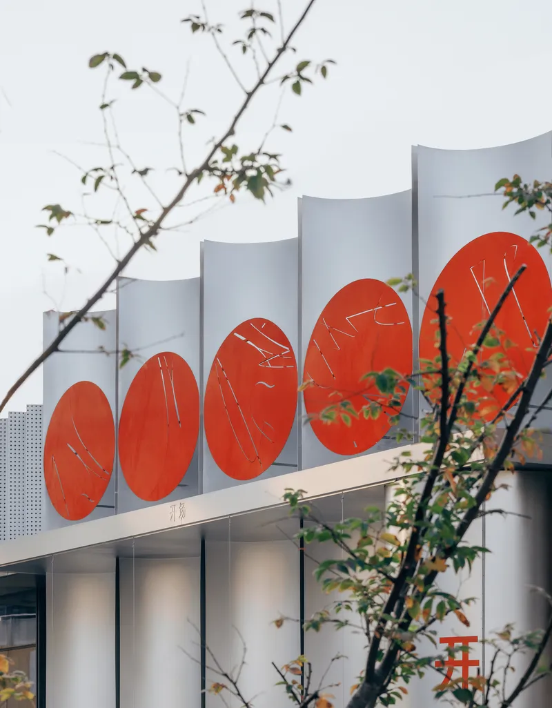 White curved roof fins above red circular graphic panels, partially framed by bare tree branches
