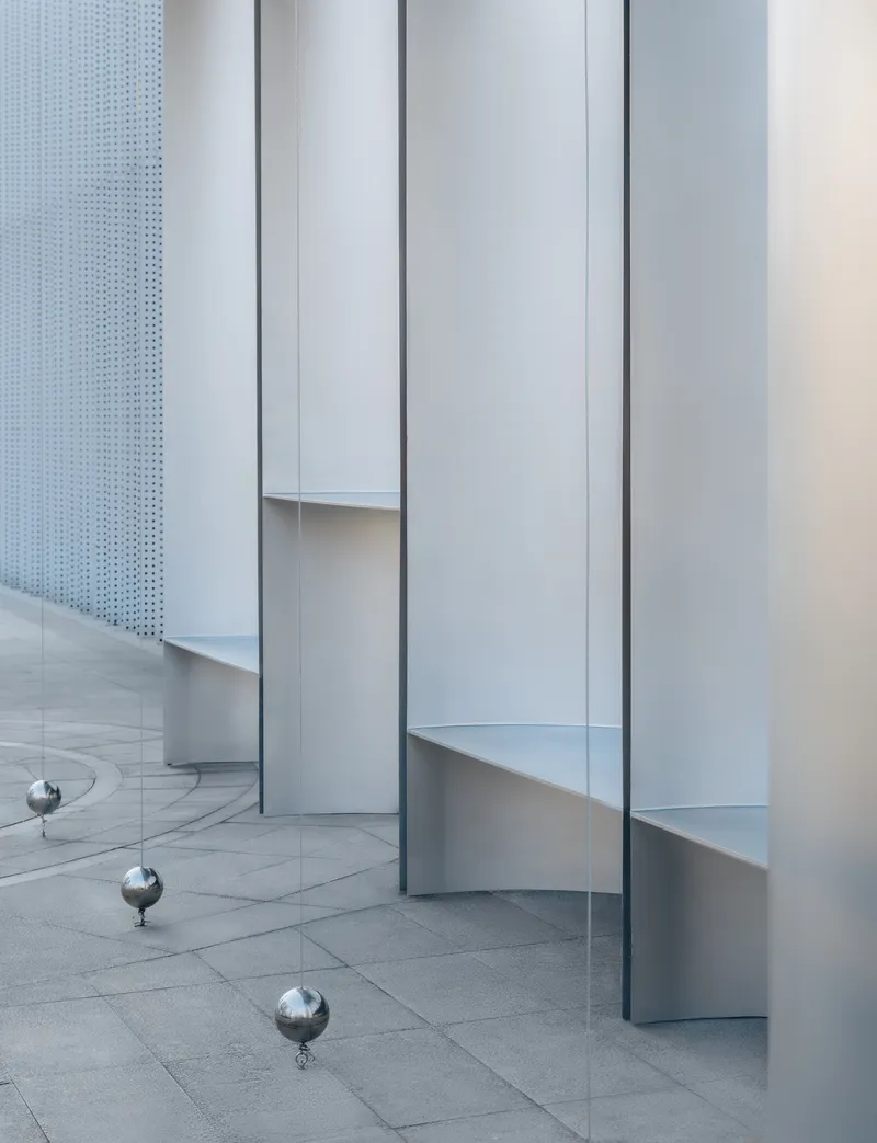 Minimalist interior with vertical white panels, perforated metal screen, and reflective spheres on stone floor