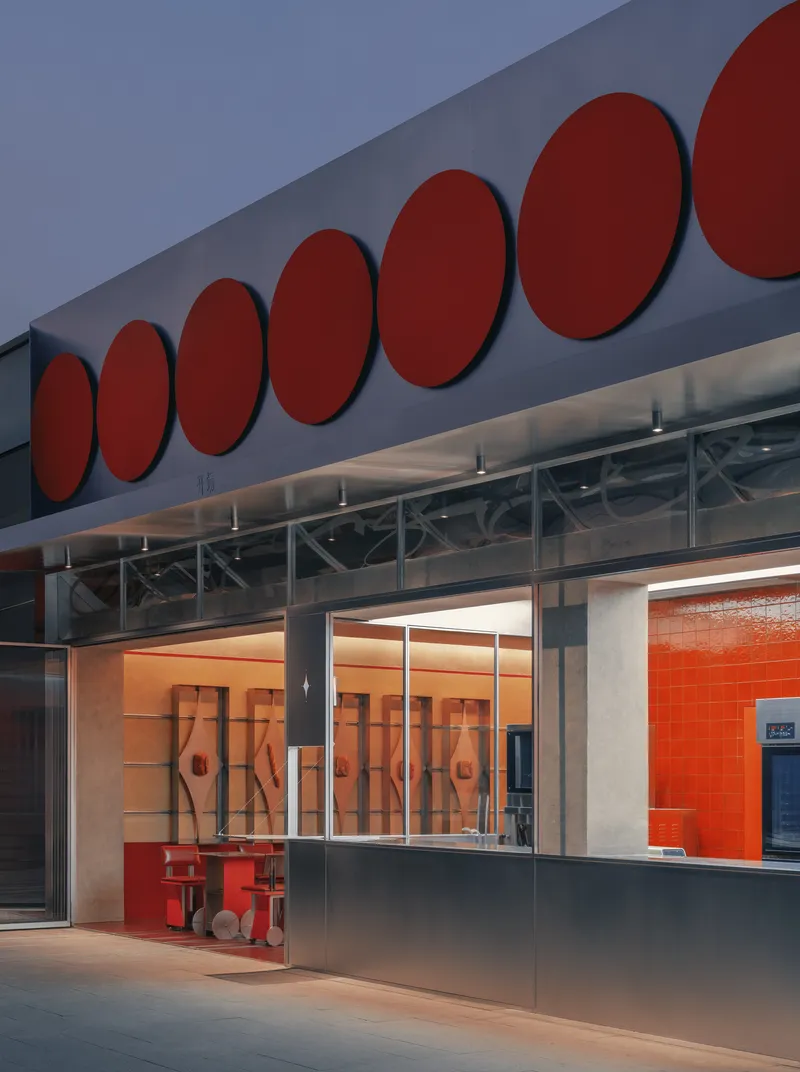 Entrance facade with red circular motifs above glazed openings and interior lighting at dusk