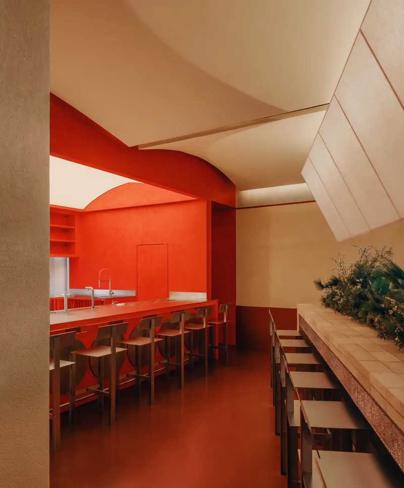 Interior dining space with red bar counter and arched opening beneath a sloped plywood ceiling