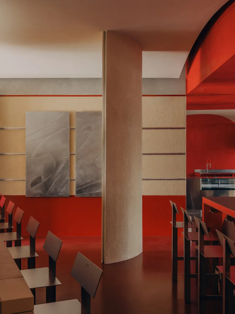 Dining area with cylindrical column, horizontal wall bands, and red resin flooring under warm light