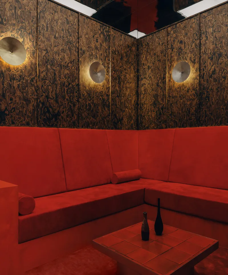 Corner banquette with red upholstery beneath decorative wood veneer walls and three disc sconces