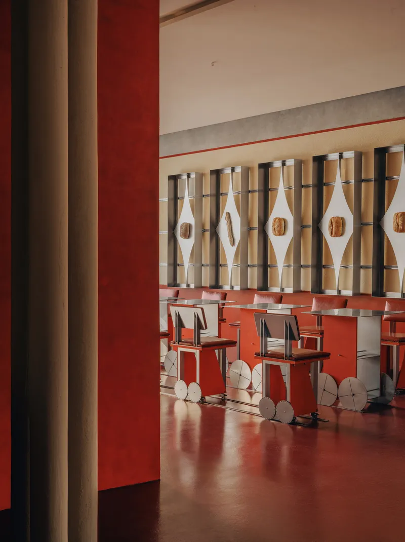View through red painted column to dining area with diamond-patterned screen and wheeled chairs