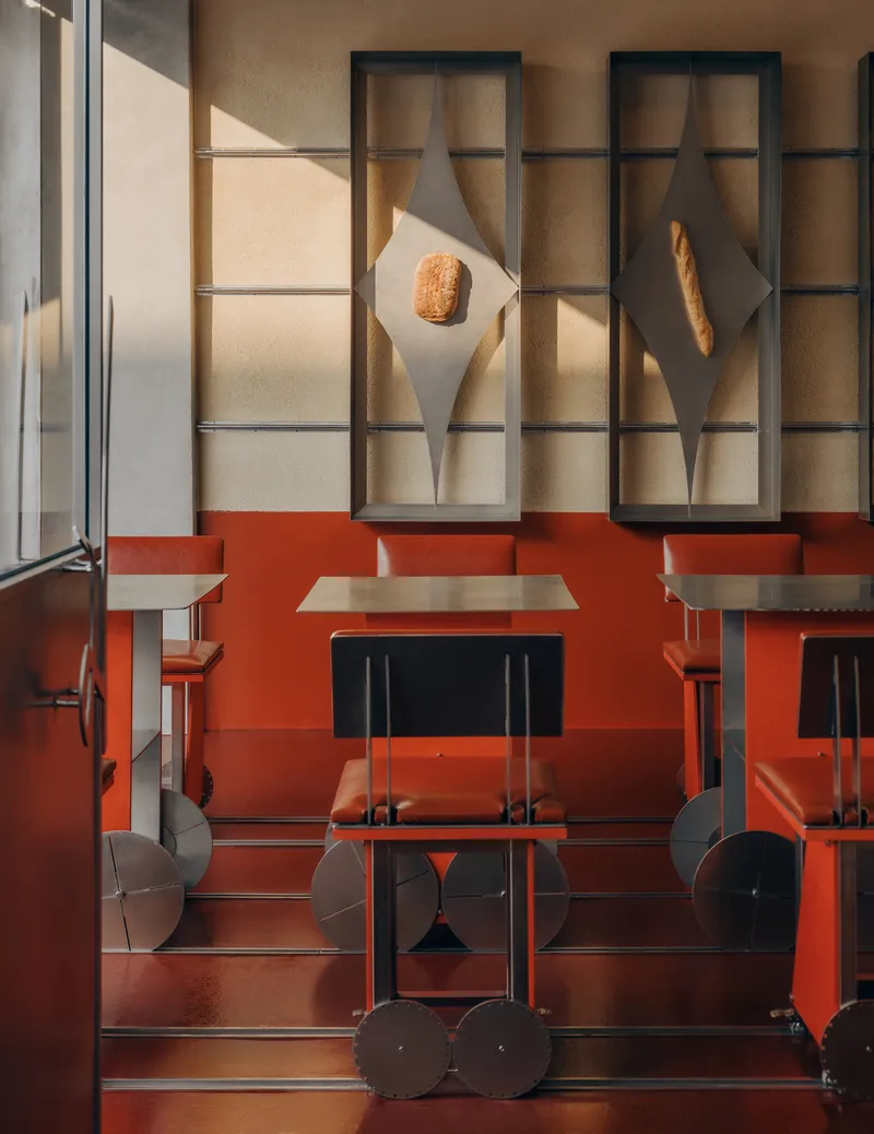Dining booth with red banquette beneath backlit display niches holding bread loaves in afternoon sun
