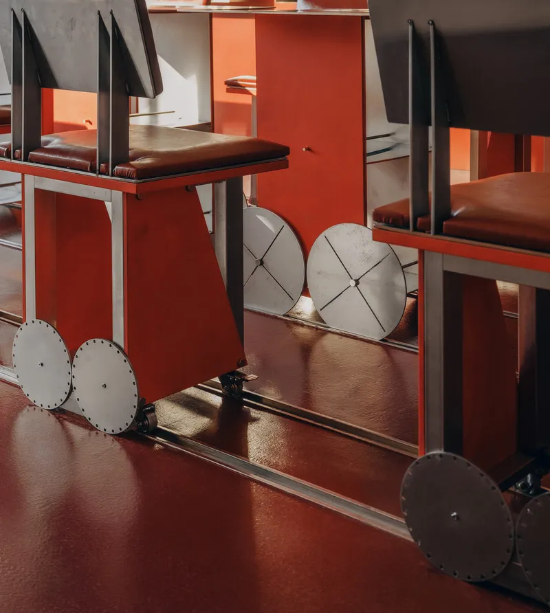 Steel-framed chairs with leather cushions and circular metal wheel details on glossy red flooring