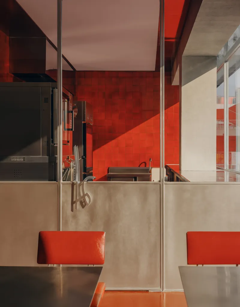 Dining area with red tile walls, stainless steel partitions, and orange banquettes beneath skylights