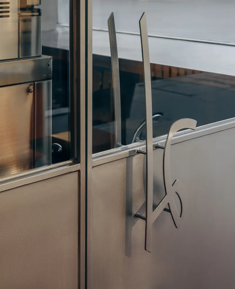 Custom door handle with fork-shaped stainless steel pull on brushed metal and glass surface