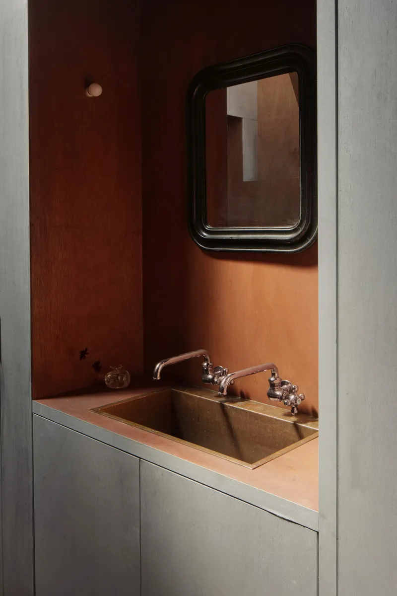 Bathroom alcove with copper sink and rounded mirror framed by grey concrete jambs