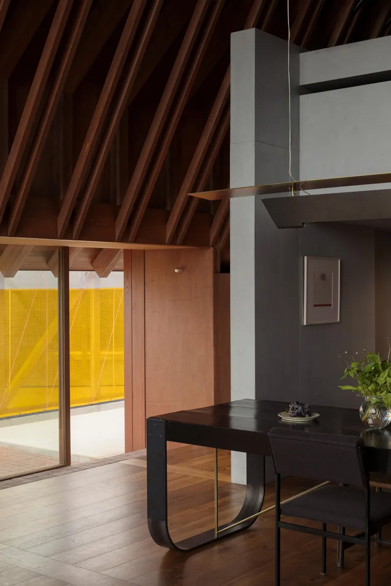 Interior with exposed timber rafters, concrete columns and sliding glass doors opening to yellow mesh courtyard