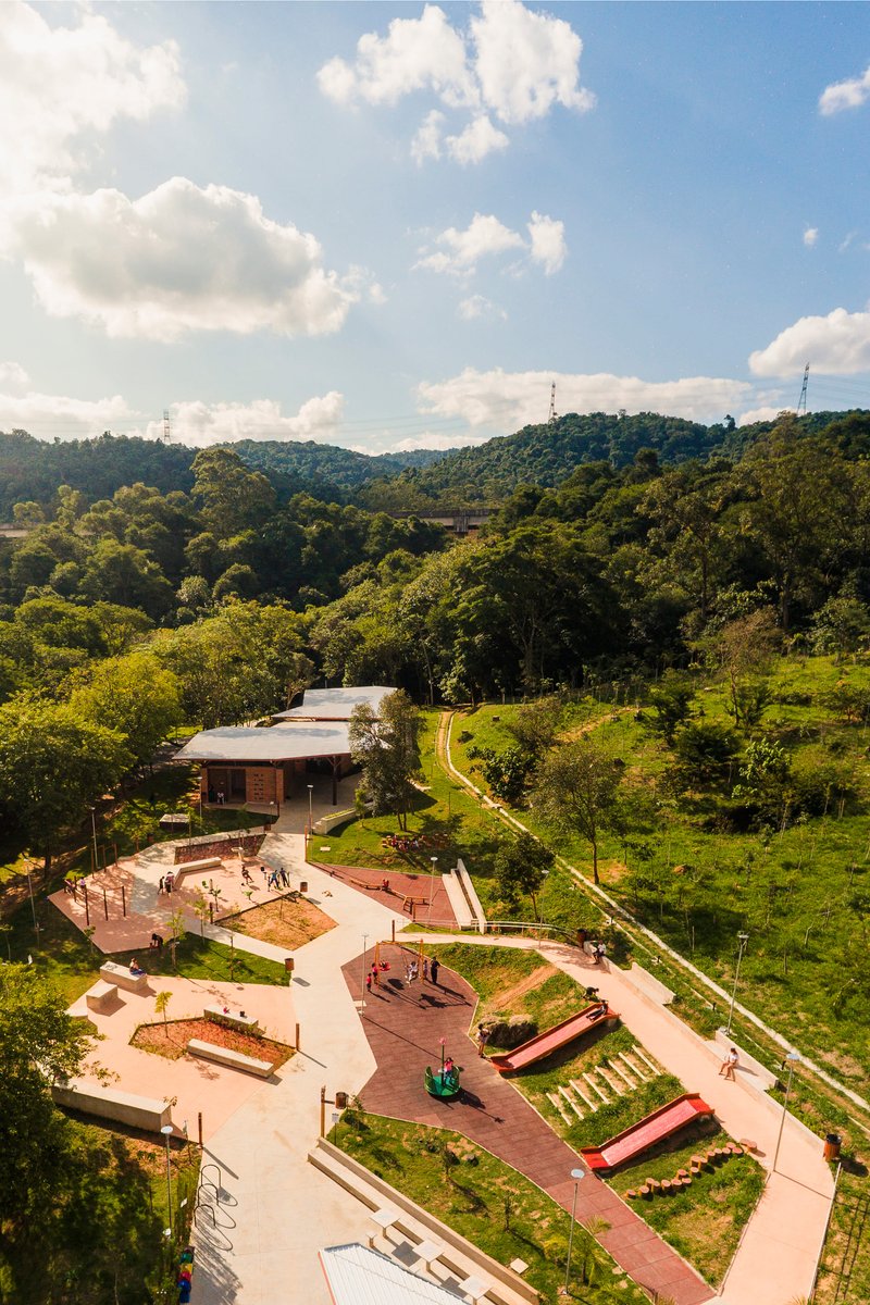 Aerial view of the playground and low-slung pavilion nestled in a forested valley below rolling hills