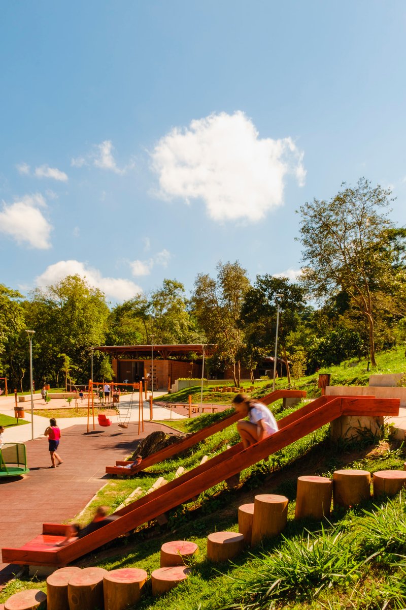 Terraced play area with angled timber ramps and cylindrical log seating under scattered clouds