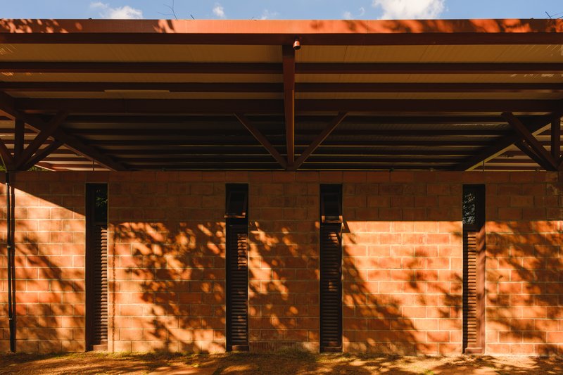 Timber pergola structure over a masonry wall with narrow vertical windows and dappled tree shadows