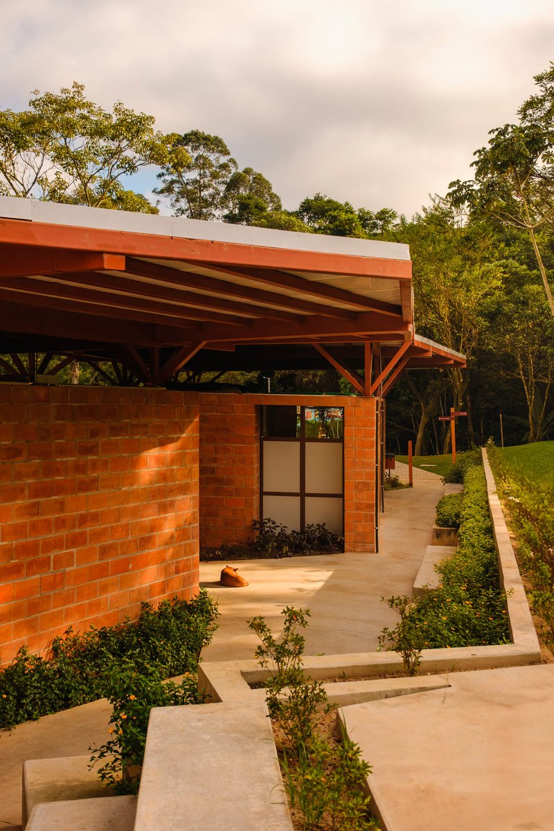 Red brick pavilion with glazed door and cantilevered roof among planted pathways at dusk