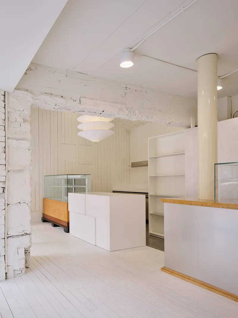 Stepped white display volume in front of an exposed white-painted stone wall