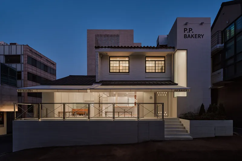 Front elevation of the converted two-storey bakery at dusk with the P.P. BAKERY signage on the side wall