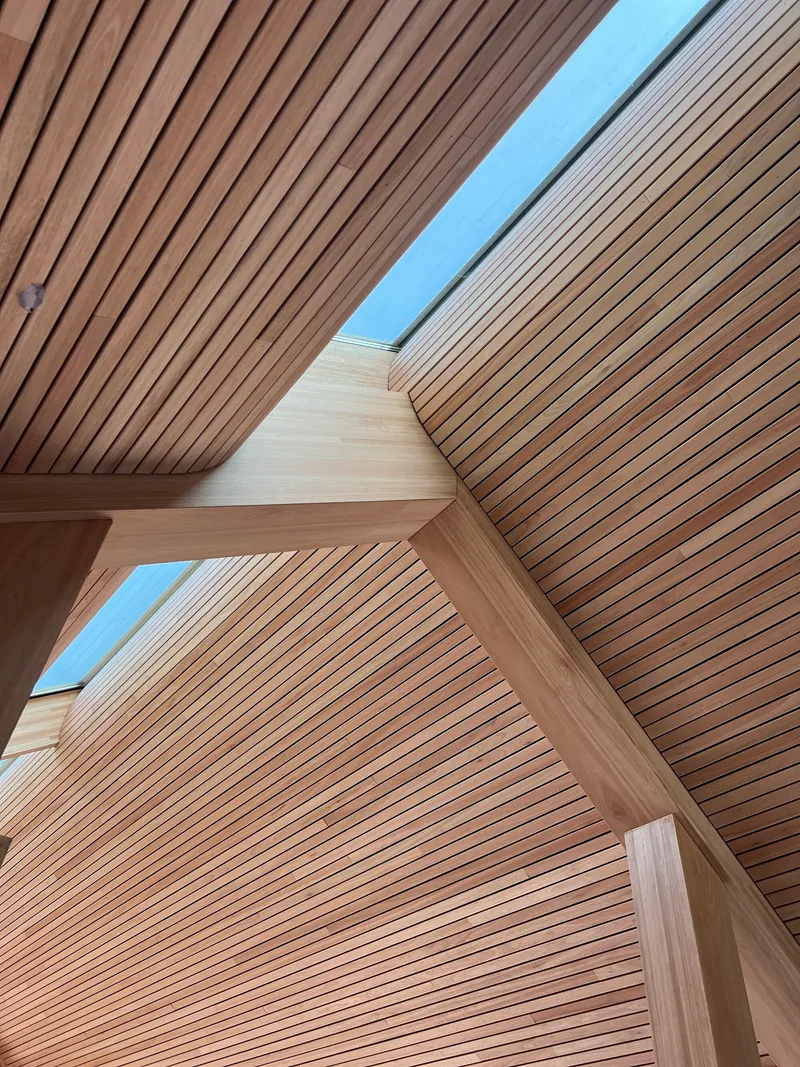 Slatted timber ceiling planes meeting at angles with narrow skylight running between them